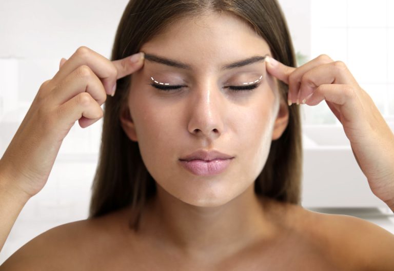 Se muestra a una mujer con los ojos cerrados, tocándose suavemente las cejas con los dedos. Parece estar demostrando un procedimiento o técnica relacionada con el tratamiento o el aumento de cejas.