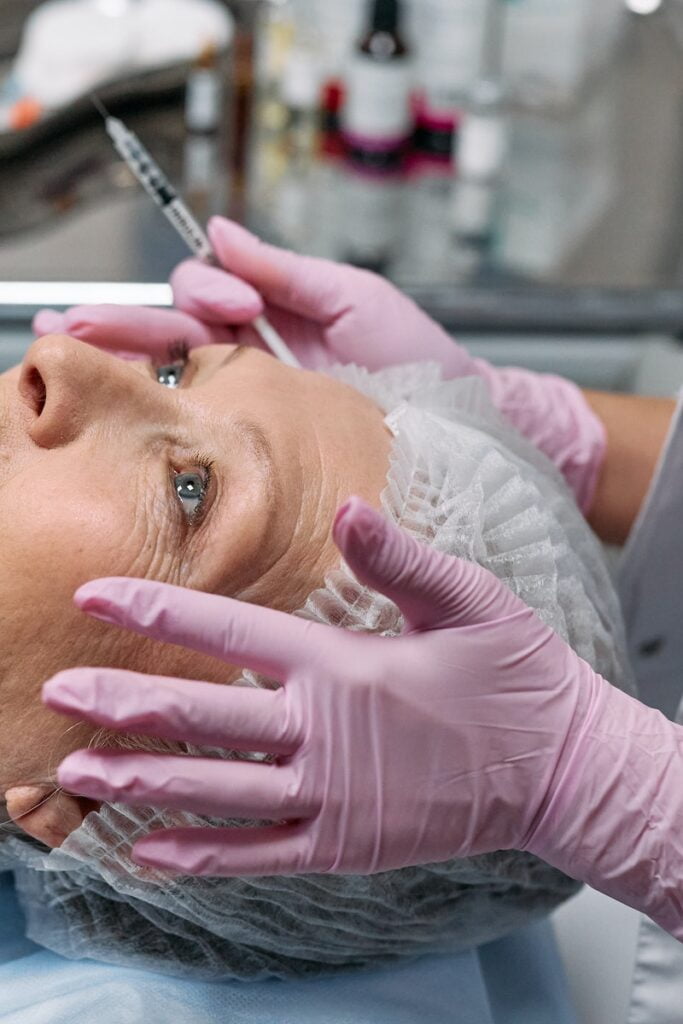 Mani che tengono il volto di una persona che indossa una cuffia da doccia, costi di botox