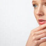 Femme avec un maquillage parfait posant touchant le menton, fond gris, recadrée, soins du visage. Jolie jeune femme avec un maquillage parfait posant touchant le menton et regardant de côté l'espace libre pour le texte sur fond gris de Studio. Panorama, recadré