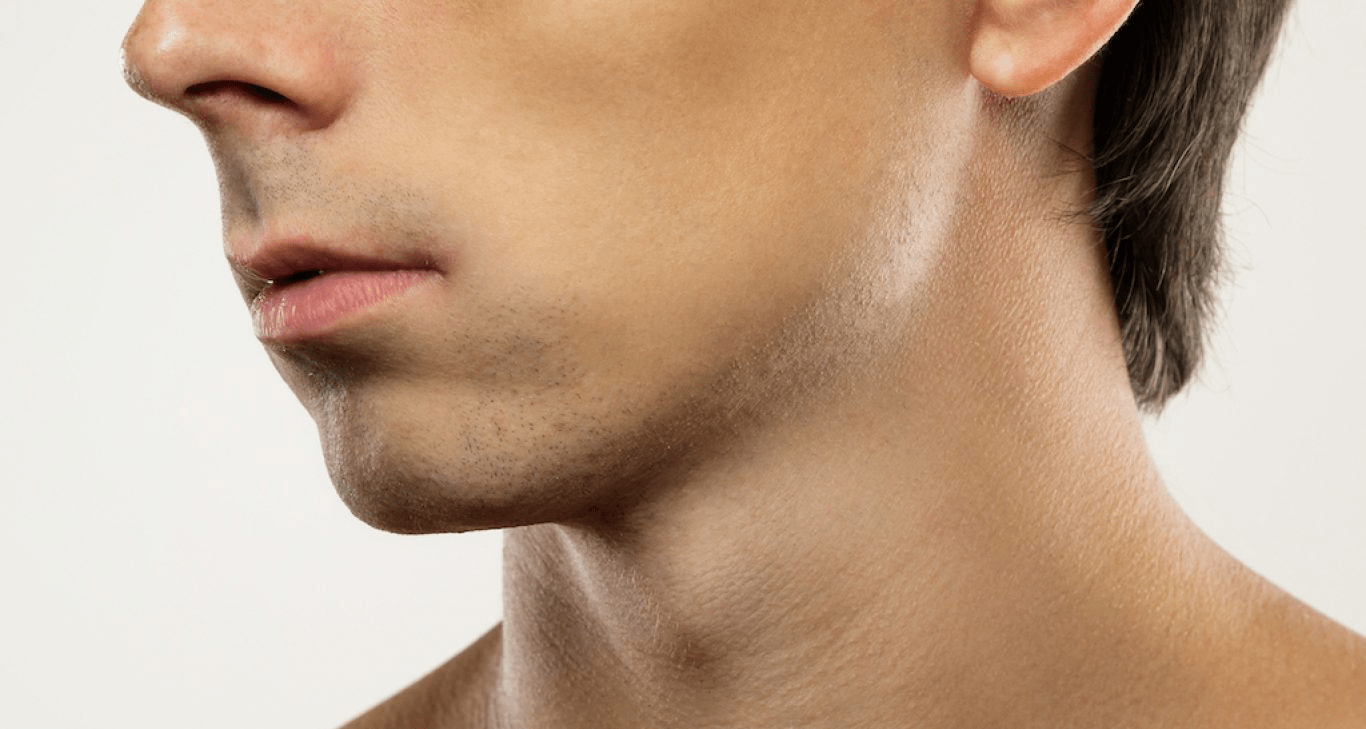 A close-up side profile of a person's face, focusing on the jawline and neck area, against a plain background. The image highlights the clean-shaven face and the smooth texture of the skin. The person's lips are slightly parted, and the side of the nose is also visible.