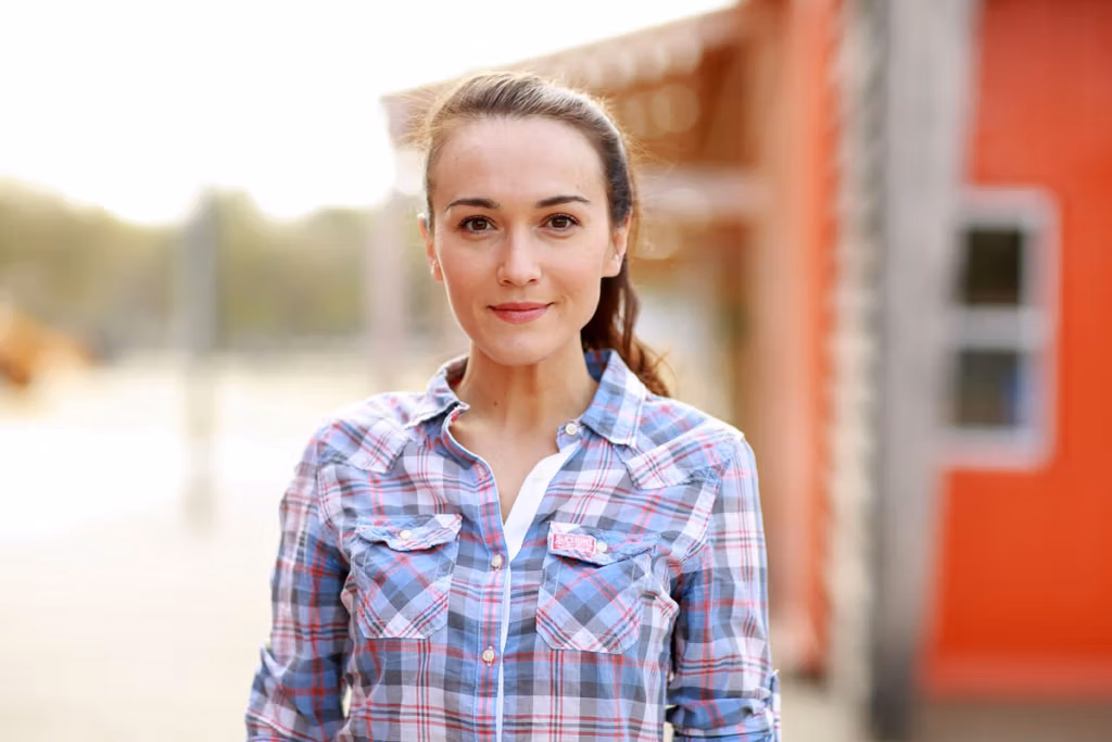 A young woman in a plaid shirt standing outdoors near a red building.