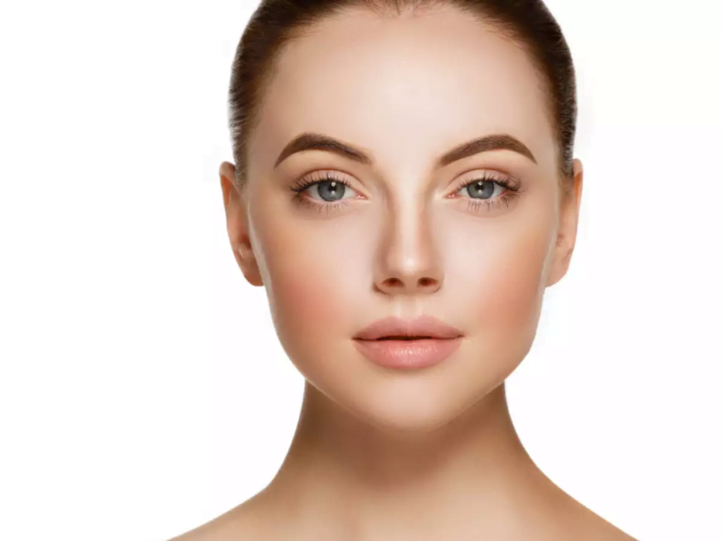 Portrait en gros plan d'une femme à la peau lisse, aux sourcils définis et à l'expression neutre, sur un fond blanc uni.