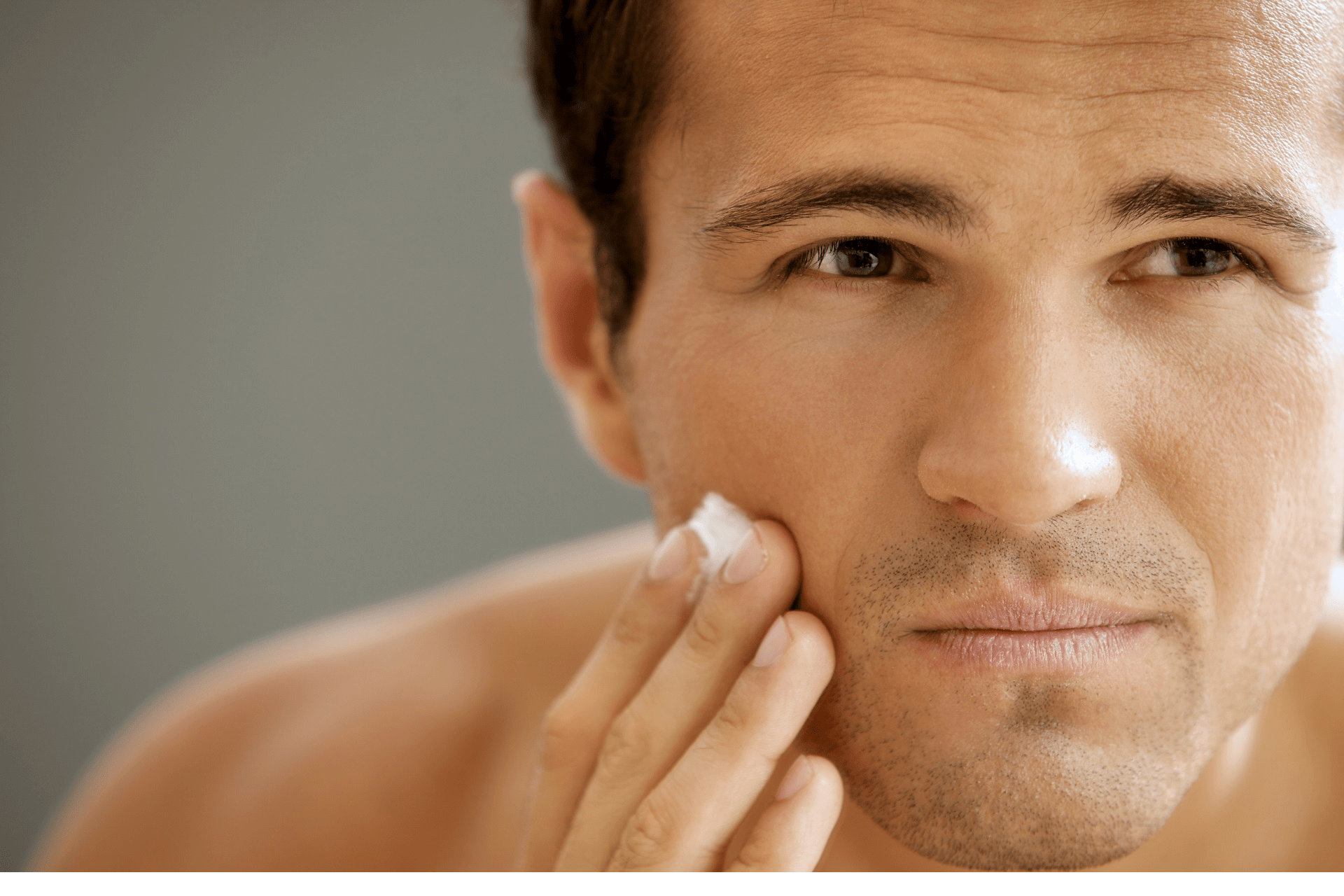 A close-up image of a man's face with visible wrinkles and aging signs, focusing on the cheek area where he is applying a skincare product with his fingers.