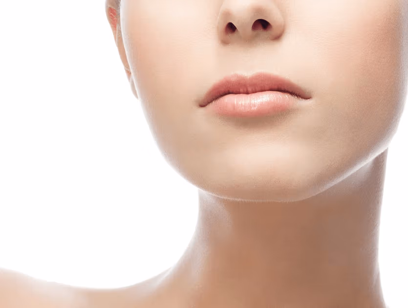 Immagine ravvicinata della parte inferiore del viso di una persona, con particolare attenzione al mento e alla zona della bocca. La pelle appare liscia e ben definita, con un aspetto morbido e naturale. Le labbra sono leggermente dischiuse, lasciando intravedere i denti. Lo sfondo è semplice e bianco, il che enfatizza i tratti del viso.