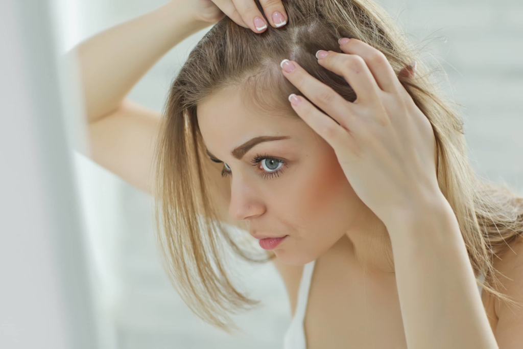 Une femme aux cheveux châtain clair vérifie son cuir chevelu, peut-être à la recherche de signes d'amincissement des cheveux ou de pellicules.