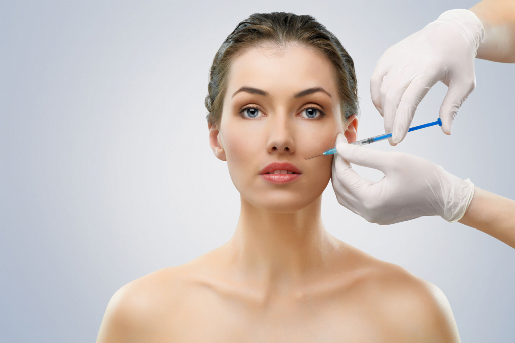 A woman receiving a cosmetic injection on her face, likely a dermal filler or Botox treatment, administered by a healthcare professional wearing gloves.