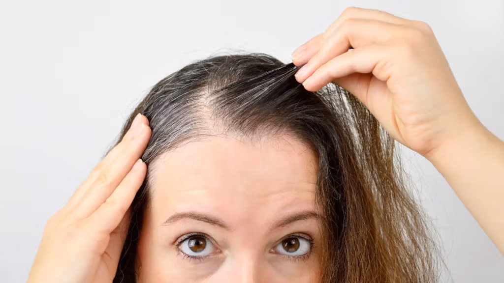 A woman examining her hair, showing signs of graying at the roots.