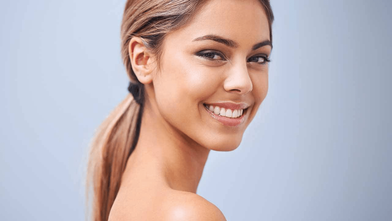 A close-up portrait of a smiling woman with smooth skin and a ponytail, showcasing her natural beauty and healthy appearance.