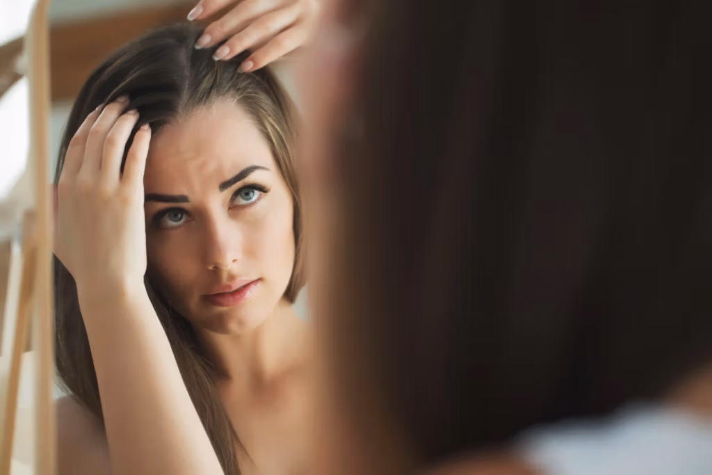 A woman looking at her hair with concern in a mirror