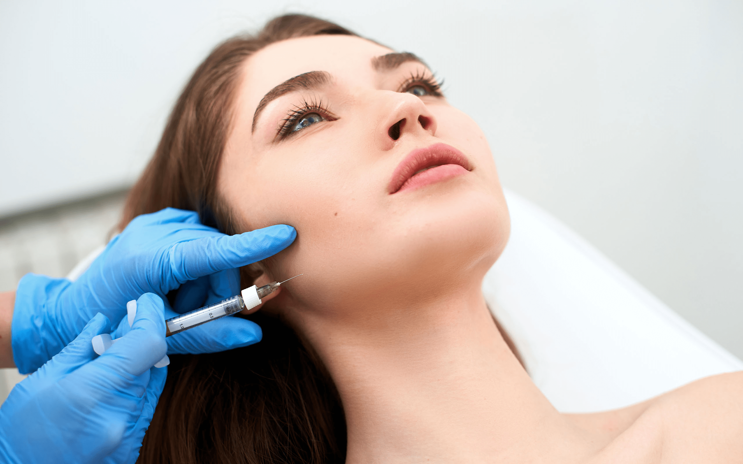 Una mujer recibe una inyección cosmética en la mandíbula por parte de un profesional médico que lleva guantes azules.