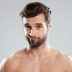 Een man zonder shirt, met een baard en kort donker haar, kijkt met een neutrale uitdrukking rechtstreeks in de camera.