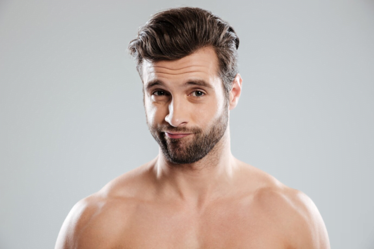 Un hombre sin camisa, con barba y cabello corto y oscuro, mira directamente a la cámara con una expresión neutra.