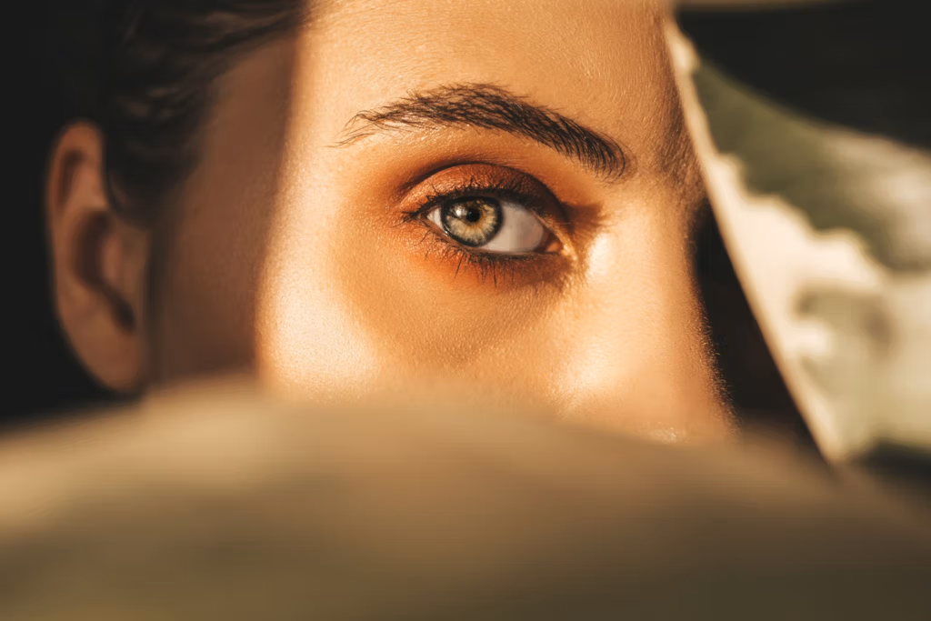 A close-up photograph of a person's face, focusing on a single visible eye. The lighting is soft and warm, casting gentle shadows and highlighting the details of the skin and eye. The person's expression is calm and contemplative, with the rest of the face partially obscured by darkness. The image conveys a sense of serenity and introspection.