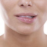 Gros plan du bas du visage, mettant l'accent sur les lèvres et le menton. Les lèvres paraissent humides et légèrement brillantes, tandis que la peau du menton et de la zone environnante est lisse, avec quelques pores visibles. L'arrière-plan, uni et blanc, souligne les traits du visage.