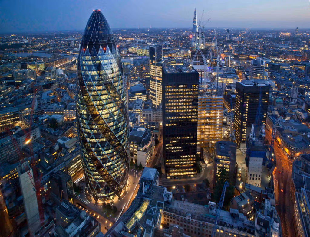 Una vista panorámica del horizonte de Londres al atardecer, con el emblemático edificio Gherkin destacando en el centro, rodeado de rascacielos iluminados y las luces de la ciudad.