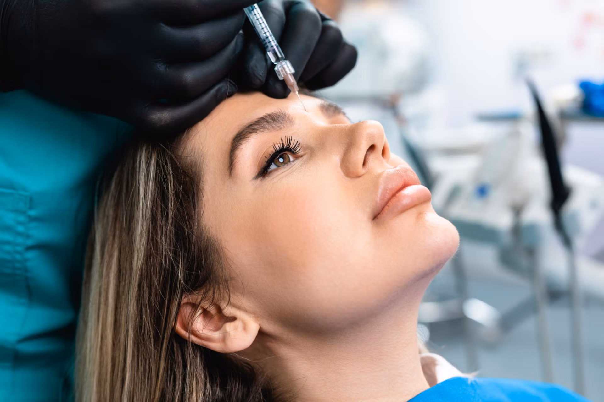 A medical professional administering an injection to a patient's forehead in a clinical setting.