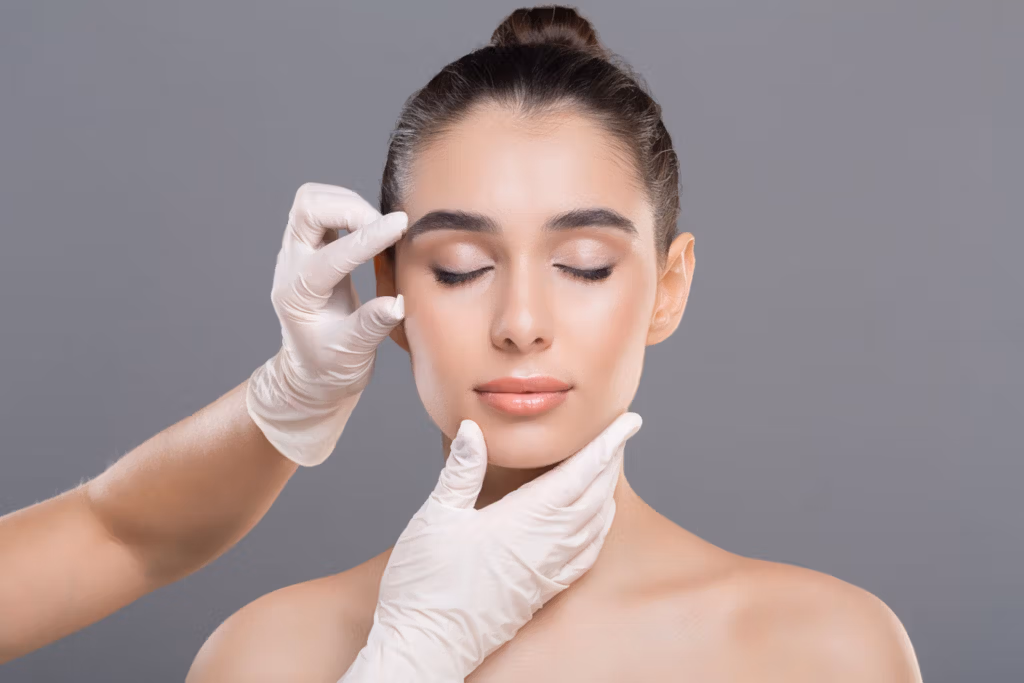 A woman receiving a facial examination or treatment from a gloved professional, with the professional's hands gently touching her cheek and forehead.