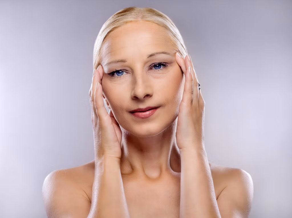 A woman with blonde hair is shown with her hands gently touching her temples, likely demonstrating a facial exercise or skincare technique.
