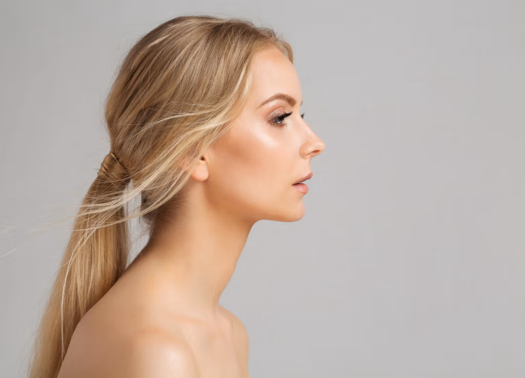 Profil d'une femme aux longs cheveux blonds, coiffés en queue de cheval basse, le regard droit devant elle, l'expression neutre. Le fond uni et clair met en valeur ses traits et la simplicité du décor.