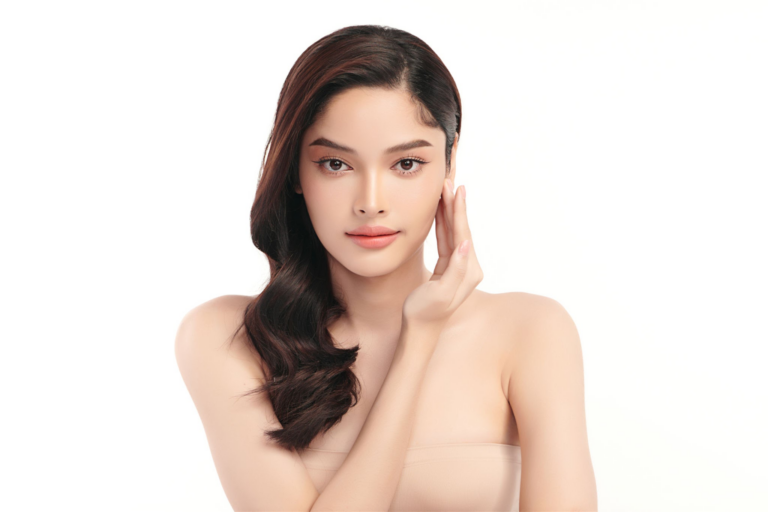 Una mujer joven con cabello largo y oscuro posando con la mano en la cara, vistiendo ropa mínima y sobre un fondo blanco liso.