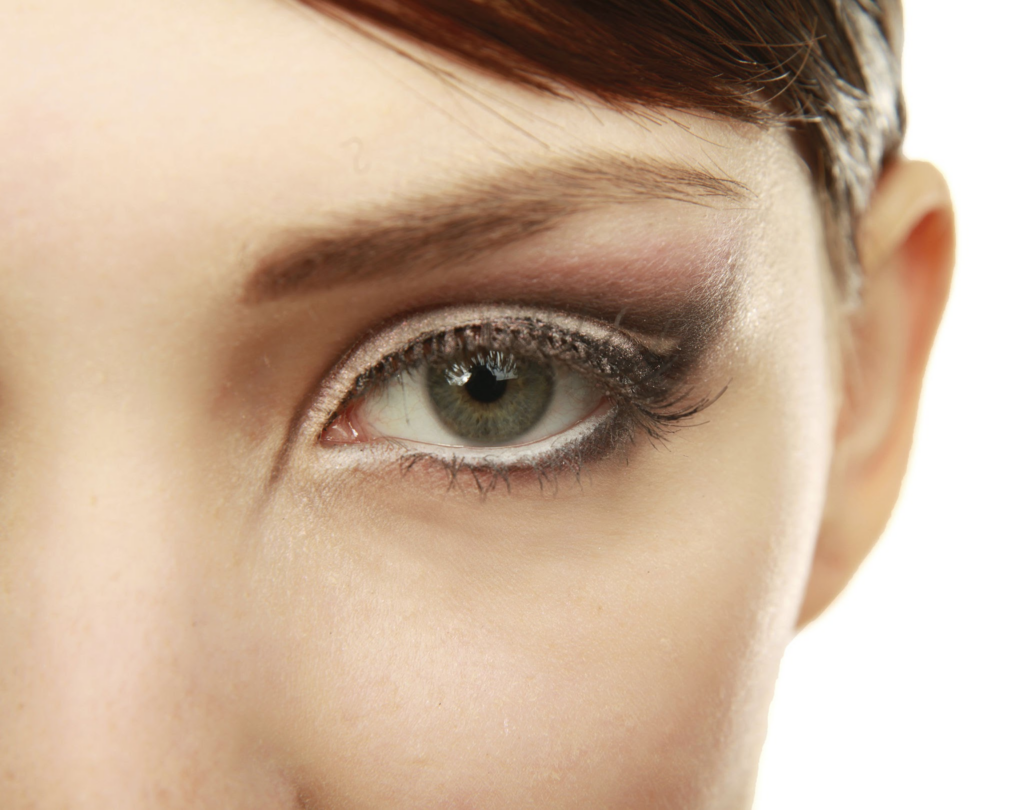 Eine Nahaufnahme des Auges einer Person mit detailliertem Make-up, mit rauchigem Lidschatten-Look, langen Wimpern und einem Hauch von Glitzer auf dem Augenlid.