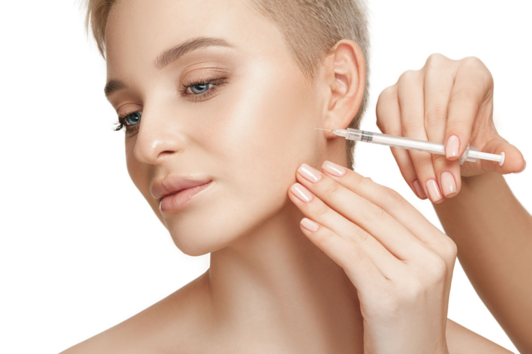Una persona con cabello corto sostiene una jeringa cerca de su cara, aparentemente administrando una inyección.