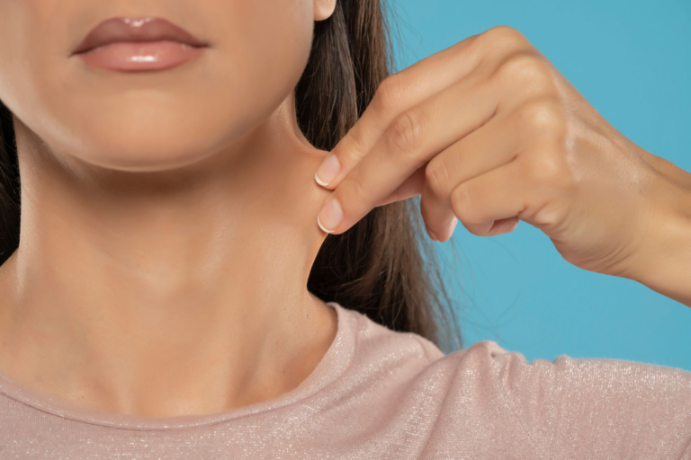 Una fotografía de cerca de una mujer tocándose el cuello, vestida con una camisa rosa y un fondo azul.