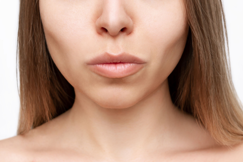 A close-up image of a woman's lower face, showcasing a smooth and youthful appearance of the lips, chin, and jawline on a clean, neutral background.