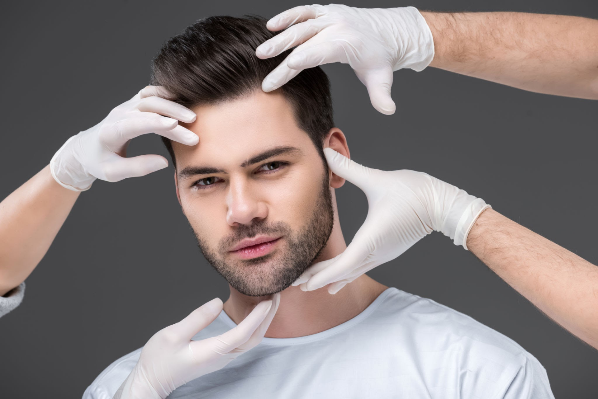 رجل يتلقى قياسات الوجه من أيادي متعددة مرتدية قفازات، على الأرجح في إطار إجراء طبي أو تجميلي.