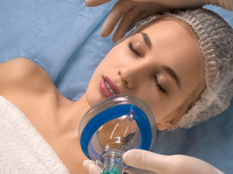 Una mujer se somete a un procedimiento médico, con un gorro para el cabello y sosteniendo una máscara de anestesia en su cara mientras está acostada en una cama médica.