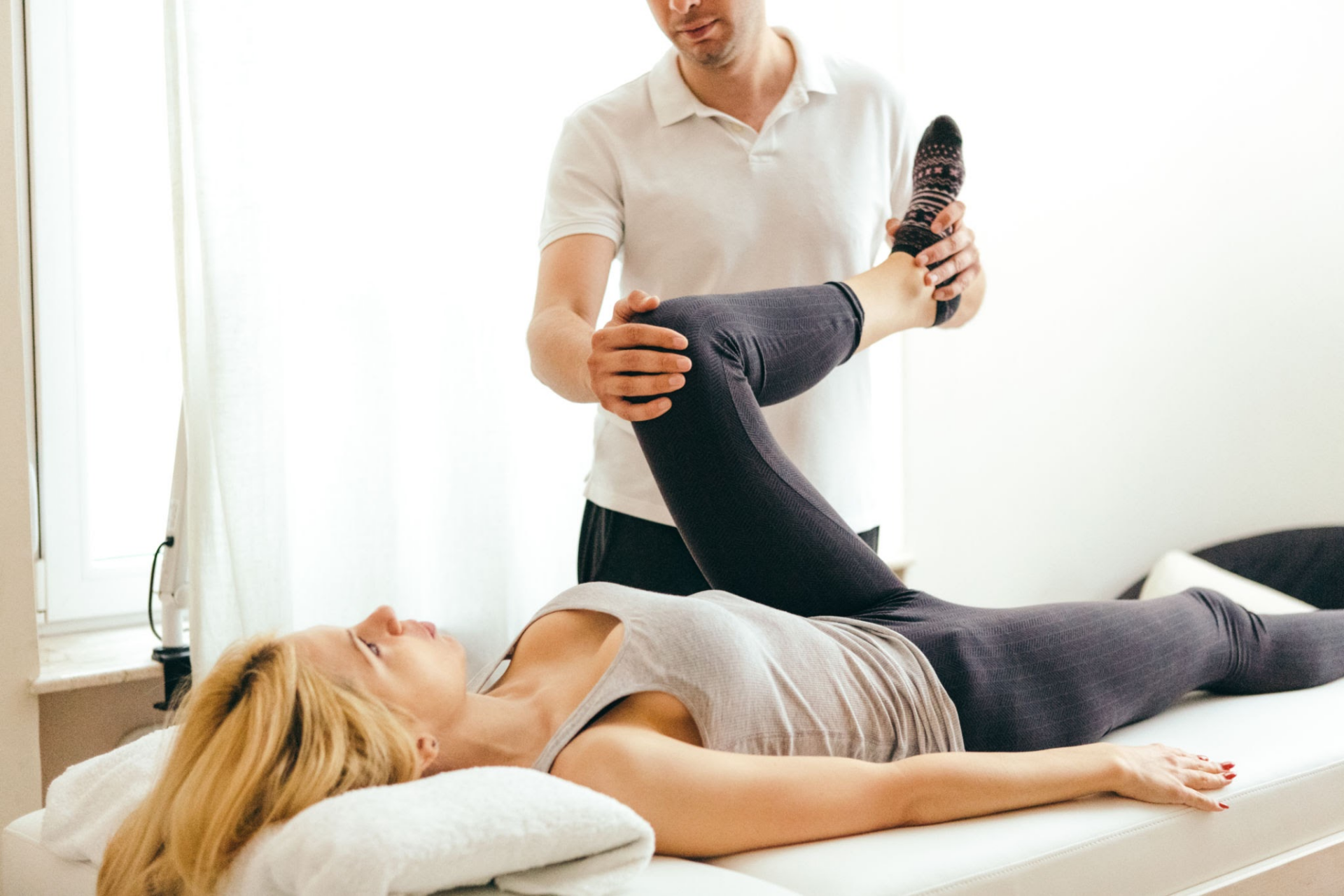 Ein Physiotherapeut hilft einer Patientin, indem er während einer Rehabilitationssitzung ihr Bein anhebt.