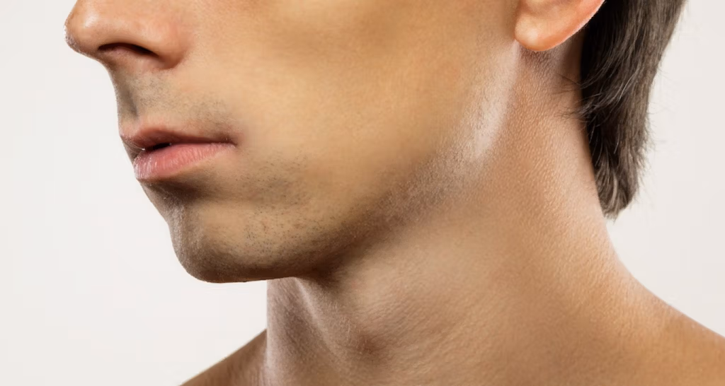 Una vista de cerca de un rostro masculino afeitado con barba visible en las mejillas y un escote suave.