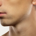 A close-up view of a shaved male face with visible stubble on the cheeks and a smooth neckline.