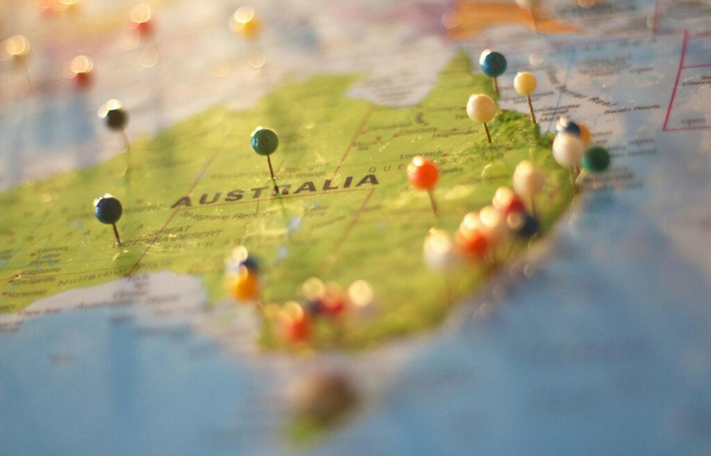 Primer plano de un mapa de Australia con alfileres de colores que marcan varias ciudades y destinos.