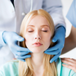 Two medical professionals in scrubs and gloves carefully examining a patient's face, likely in a clinical setting.
