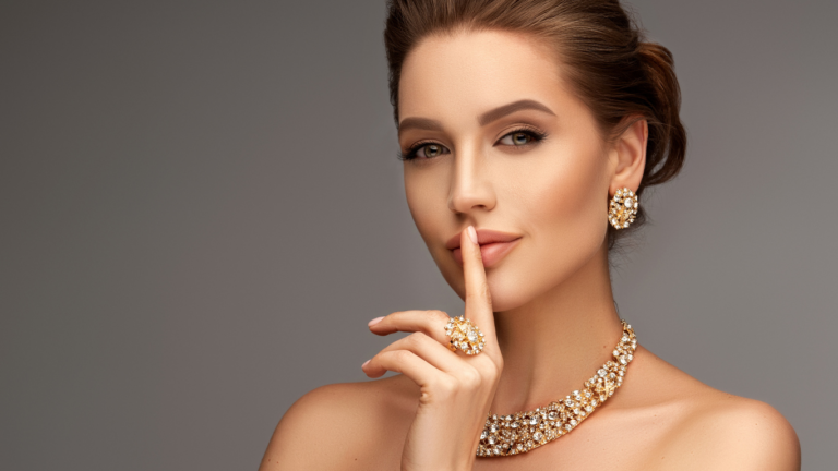 Una mujer con maquillaje elegante y joyas haciendo un gesto de silencio.