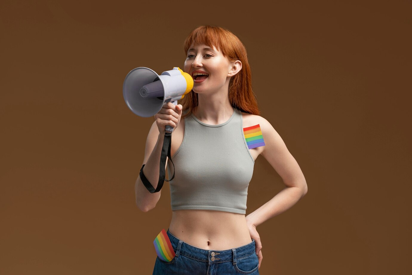 A confident woman with a rainbow flag on her shoulder, speaking into a megaphone, representing LGBTQ+ pride and advocacy.