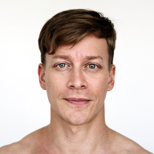 A close-up portrait of a young man with short brown hair, facing the camera with a neutral expression, on a plain white background.