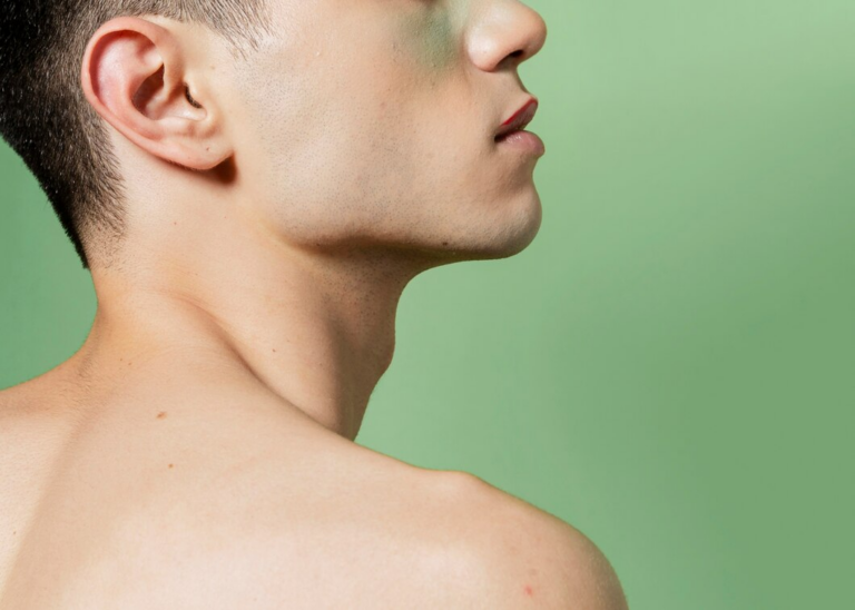 Perfil lateral de un hombre con la cara bien afeitada y cabello corto, mirando hacia arriba contra un fondo verde claro.
