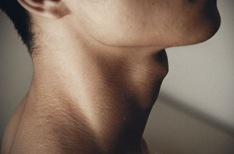 Primer plano del cuello y la mandíbula inferior de una persona con vello facial corto, resaltando la textura de la piel sobre un fondo liso.