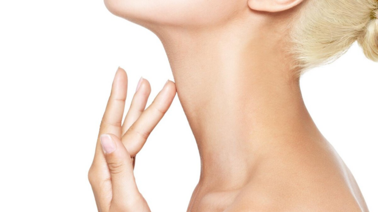 Primer plano del cuello y la mano de una mujer. La mujer se toca suavemente el cuello con las yemas de los dedos, posiblemente buscando signos de envejecimiento o alguna condición de la piel. La atención se centra en la suavidad y textura de la piel, destacando la zona del cuello.