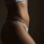 Gros plan du torse d'une personne portant un vêtement blanc avec une ceinture élastique visible sur un fond sombre.