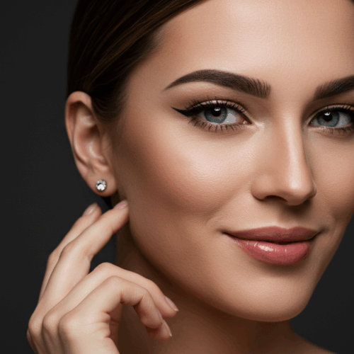 Gros plan d'une femme aux cheveux châtain clair tirés en arrière, au maquillage discret et portant une boucle d'oreille en diamant. Elle a les yeux verts, des sourcils bien dessinés et un sourire doux. L'arrière-plan sombre met en valeur les traits de son visage.