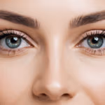 Gros plan sur le visage d'une femme, mettant en valeur ses yeux, ses sourcils et son nez. Ses yeux sont brillants et vibrants, avec des iris aux nuances de vert et de bleu. Ses sourcils sont soignés et sa peau paraît lisse et éclatante. L'image capture la beauté naturelle et l'expressivité de ses traits.