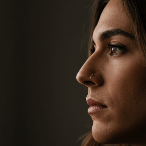 Een close-up profielfoto van een vrouw met een neusring, die opzij kijkt tegen een donkere achtergrond.