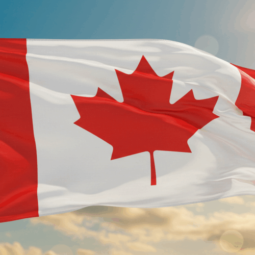 Een Canadese vlag wappert in de lucht tegen een onscherpe achtergrond van wolken.