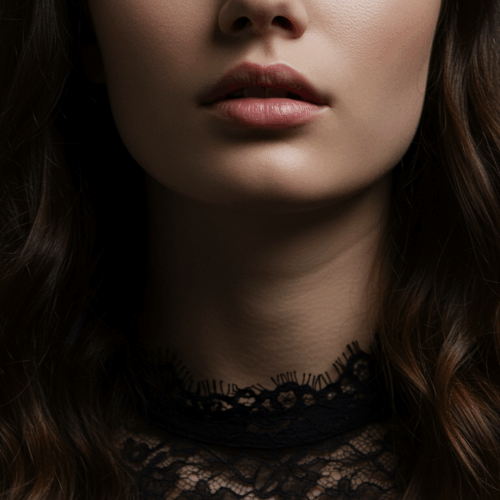 A close-up photograph of a woman's face, focusing on her lips, chin, and neck. The image is taken in low lighting, with the background in darkness, creating a dramatic effect. The woman has long, wavy hair and is wearing a black lace top. The lighting highlights her facial features, giving the image a moody and artistic tone.