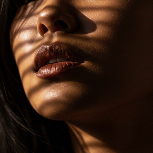 A close-up portrait of a person with warm, golden lighting highlighting their lips and cheekbones, creating a dramatic and sensual atmosphere.