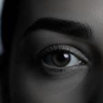 A close-up photograph of a person's eye, focusing on the intricate details of the eyelashes and the iris. The image highlights the texture of the skin and the natural beauty of the eye.