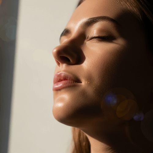 A woman with her eyes closed, appearing to be in a state of relaxation or meditation, with sunlight gently illuminating her face.